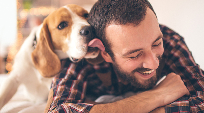 A man and his dog laying on the couch while the dog tries to lick his face