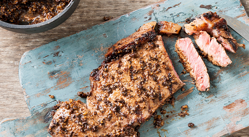 A freshly cooked pork chop on a butchers block being cut into strips