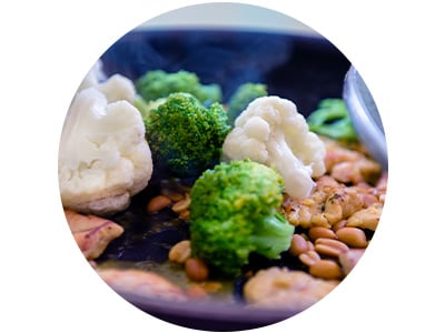 Close-up of roasted cauliflower florets and broccoli with seeds and seasonings on a dark baking surface.