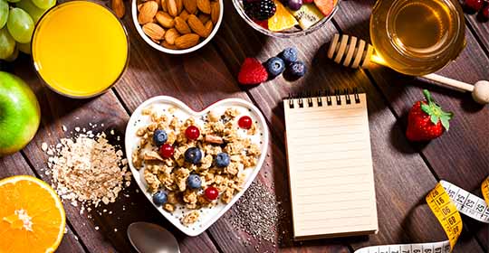 A bowl of granola cereal, various fruits and nuts on a table