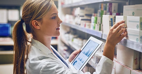 pharmacist holding tablet and looking at drugs on shelf